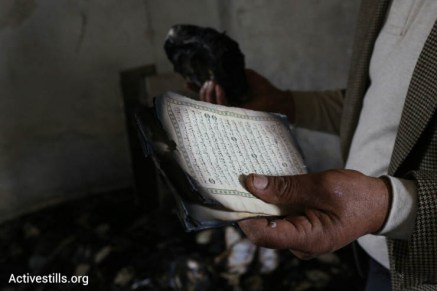A man inspects a Quran damaged in a suspected arson hate crime against a mosque in the West Bank village of Al Mughayir, November 12, 2014. (Photo by Oren Ziv/Activestills.org)